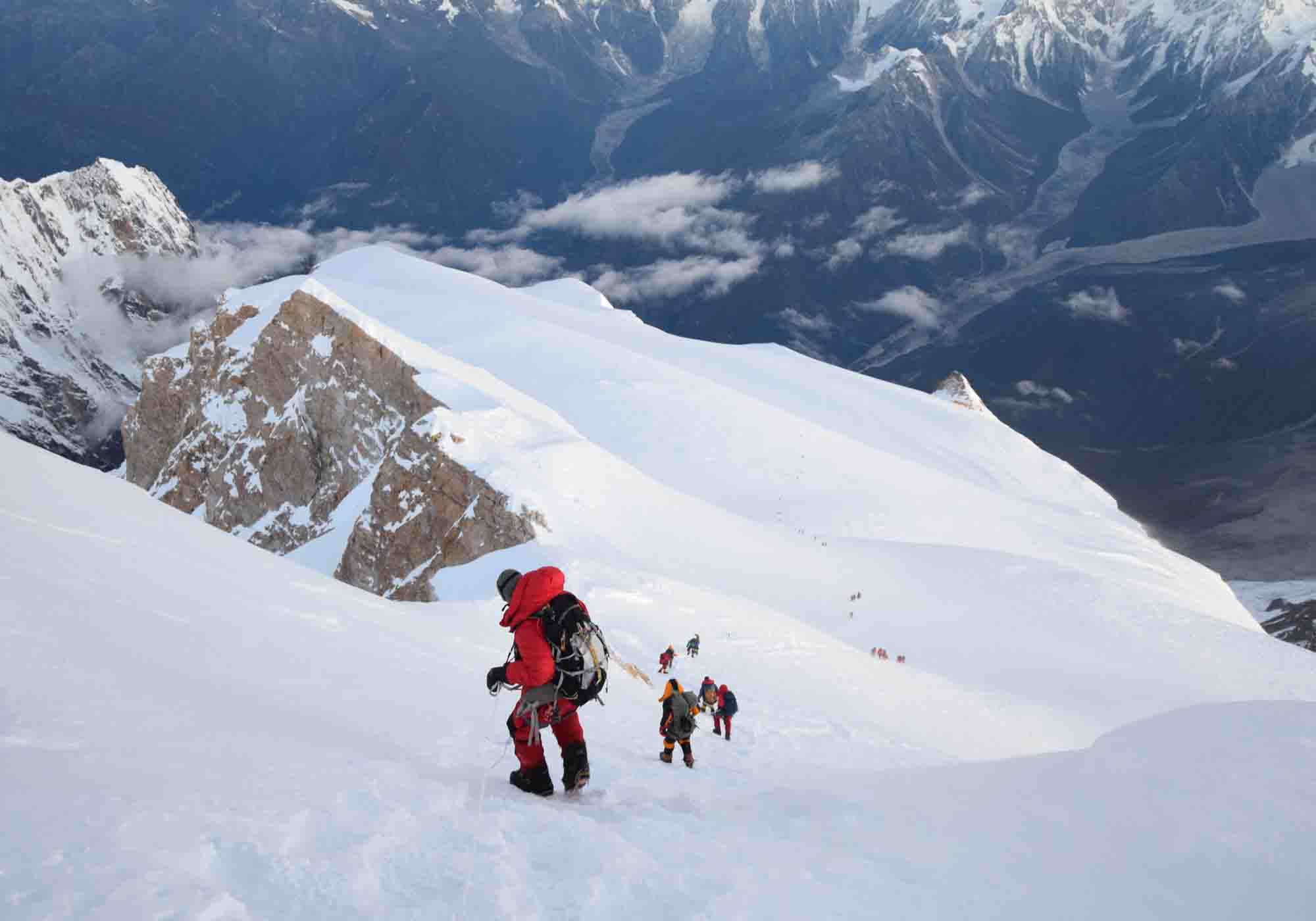 Manaslu Expedition with snow capped peak towering above rugged himalayan landscape under clear blue skies in Nepal.